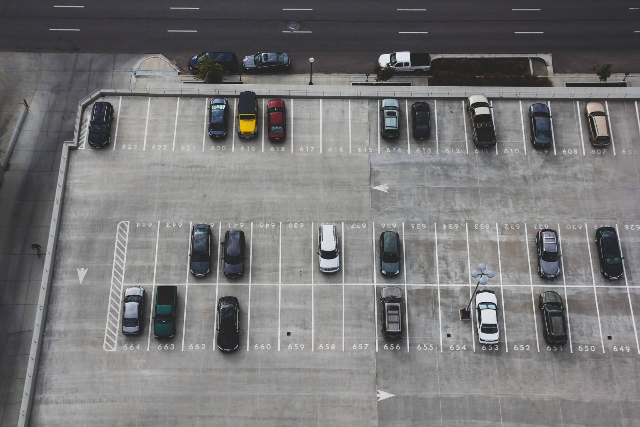 Aerial view of a mostly empty parking lot with parked cars and numbered spaces near a road.