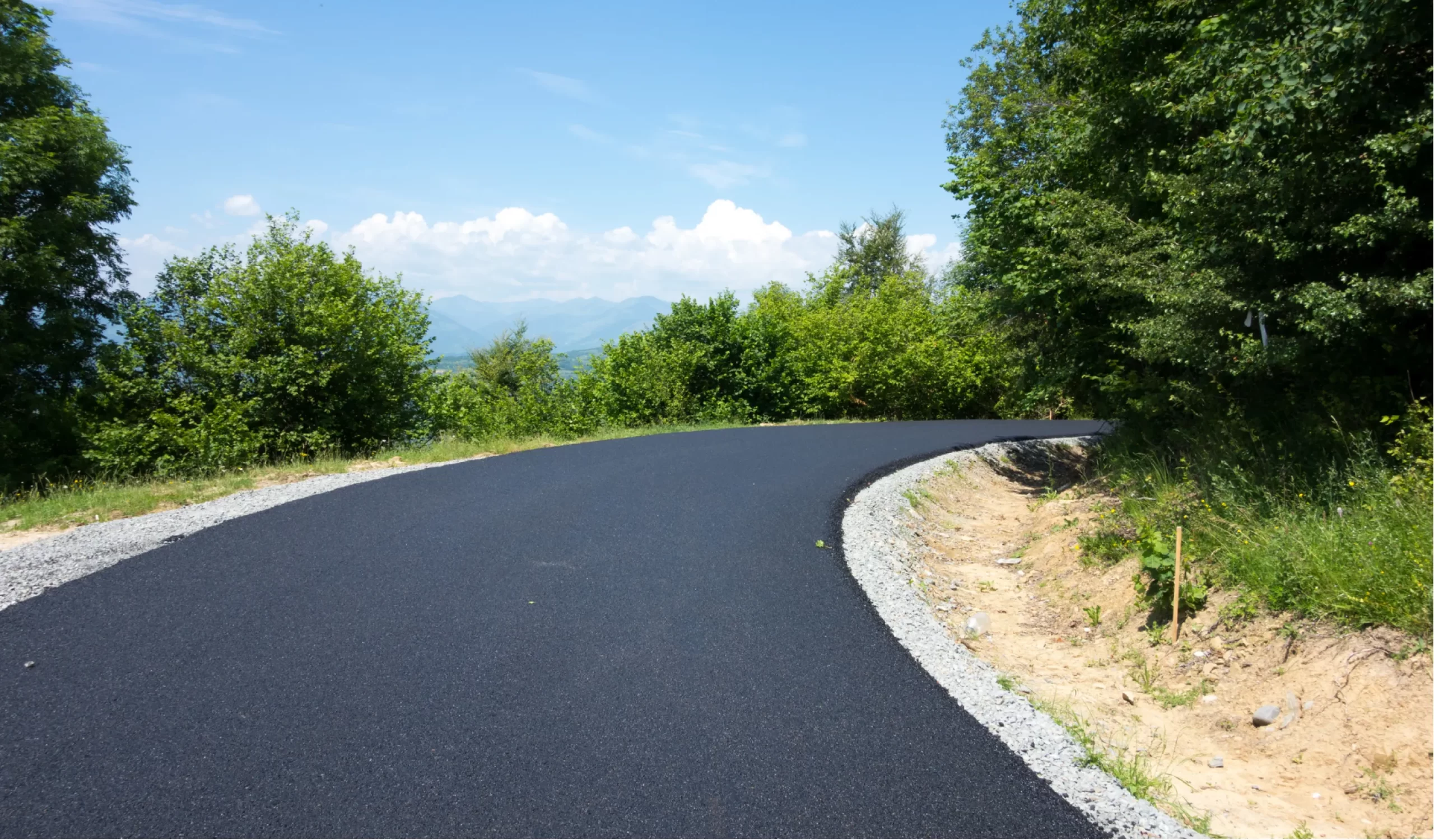 blacktop-h Freshly paved road curving through green trees on a sunny day with clear blue sky.