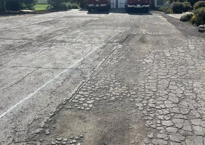 Cracked, weathered driveway leading to a house with two red trucks parked by the garage.