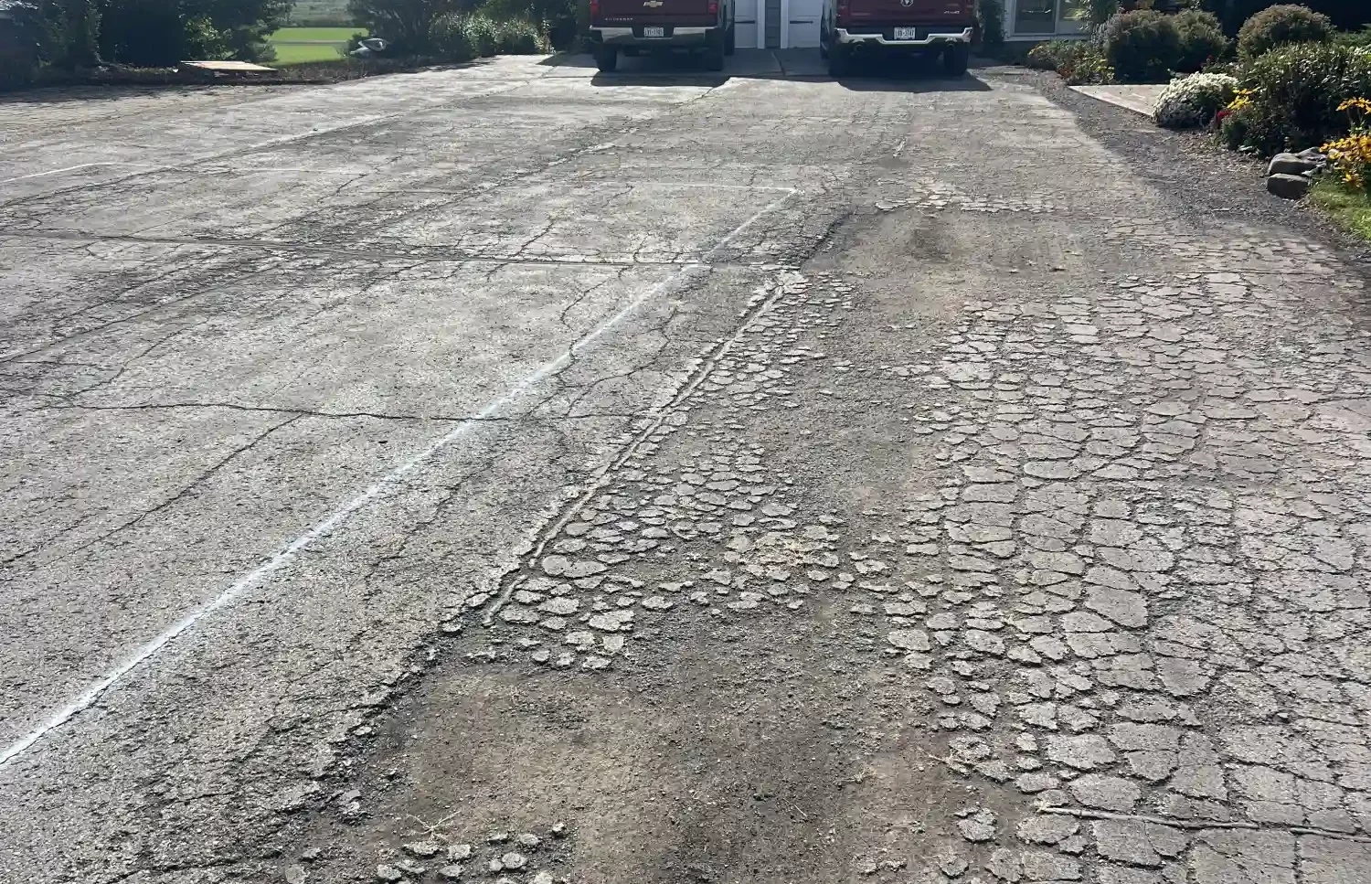 Cracked, weathered driveway leading to a house with two red trucks parked by the garage.