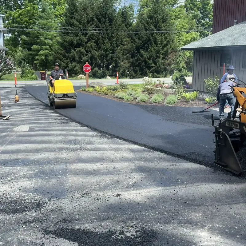 Workers paving a driveway with fresh asphalt using construction equipment on a sunny day.