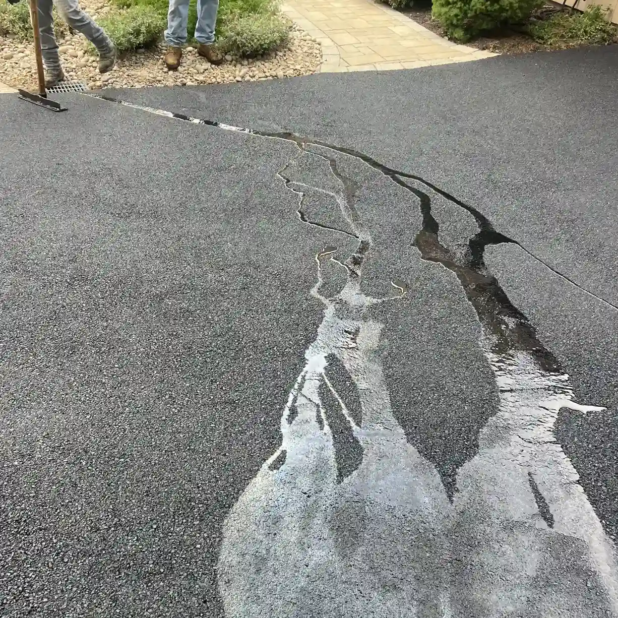 Water running along cracks in a fresh asphalt driveway, with two people standing nearby.